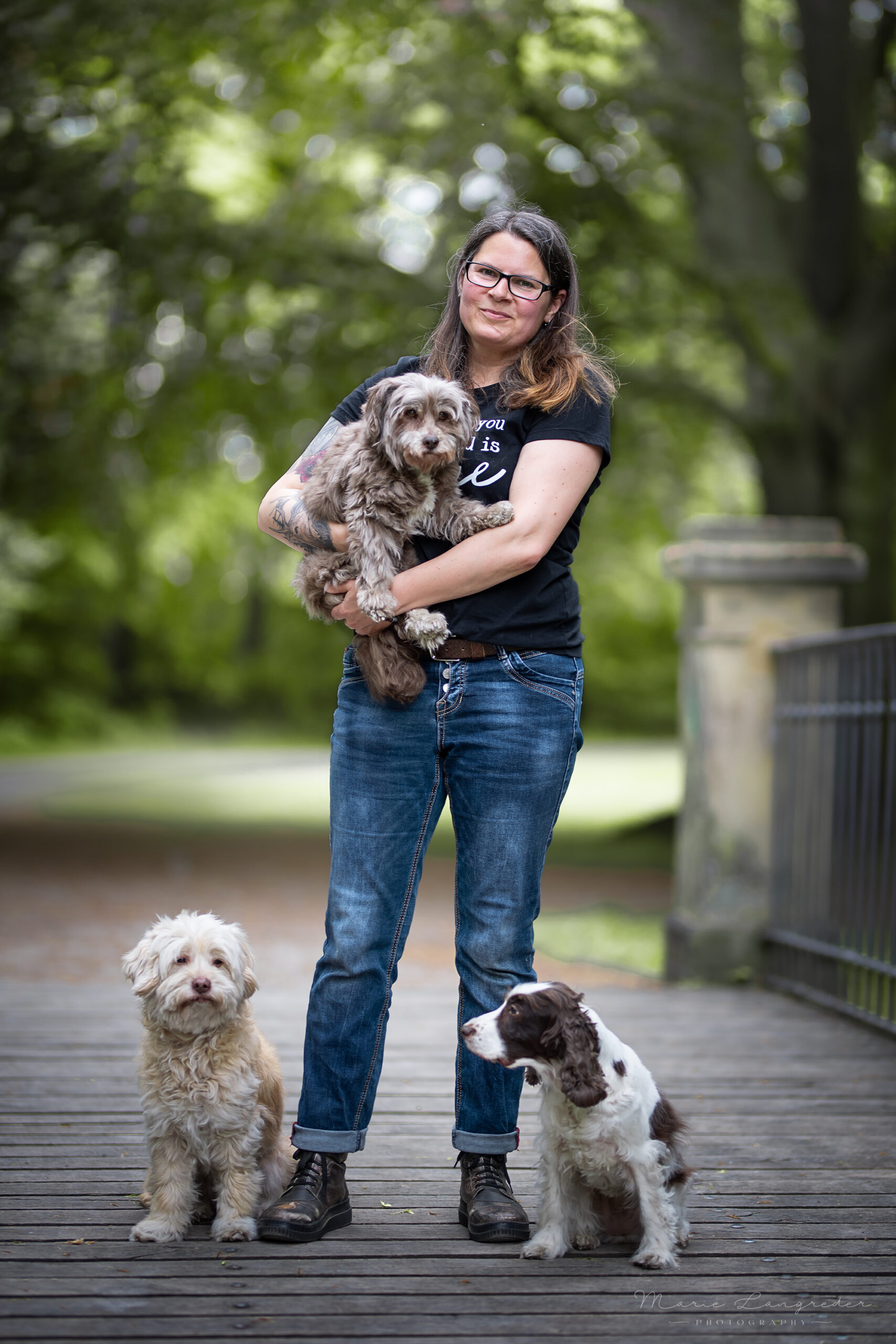 Maike Fügner steht auf einer Brücke, zwei ihrer Hunde sitzen neben ihr und einen hat sie auf dem Arm