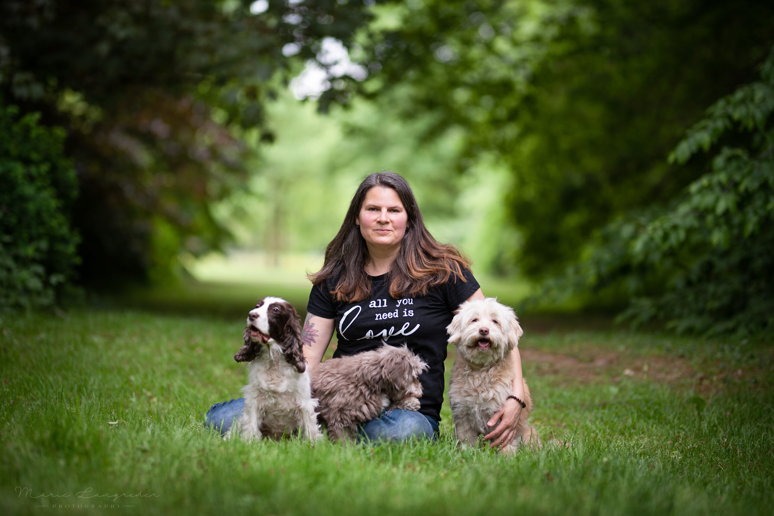 Maike Fügner mit ihren drei Hunden, auf einer Wiese mit Bäumen im Huntergrund